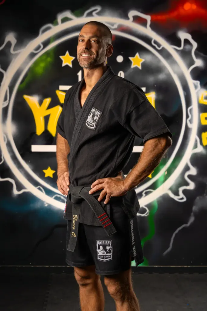 Olivier Blanco souriant, mains sur les hanches, en veste de combat
