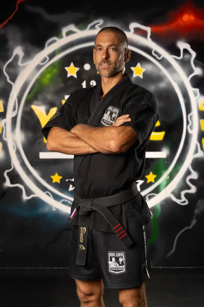 Olivier Blanco in a fight jacket and black belt, arms crossed, in the Simiane-Collongue gym